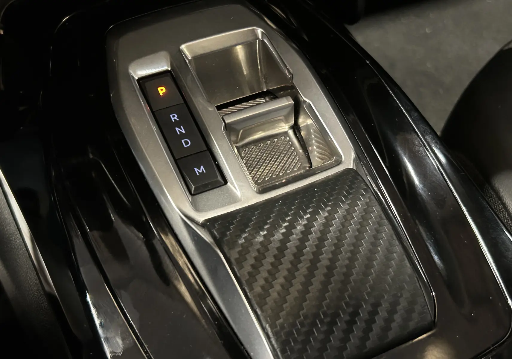 Gros plan sur la console centrale noire avec levier de vitesses automatique et finition carbone du Peugeot 2008 II Ph.2 Allure Hybrid.