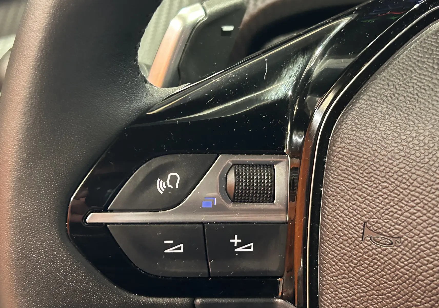Gros plan sur les commandes noires du volant du Peugeot 2008 II Ph.2 Allure Hybrid 145, détails de la molette et boutons.
