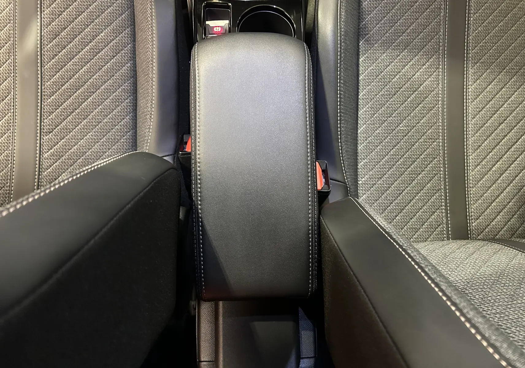 Vue plongeante sur l'accoudoir central en cuir noir et les sièges gris Selenium du Peugeot 2008 II Ph.2 Allure Hybrid 145.