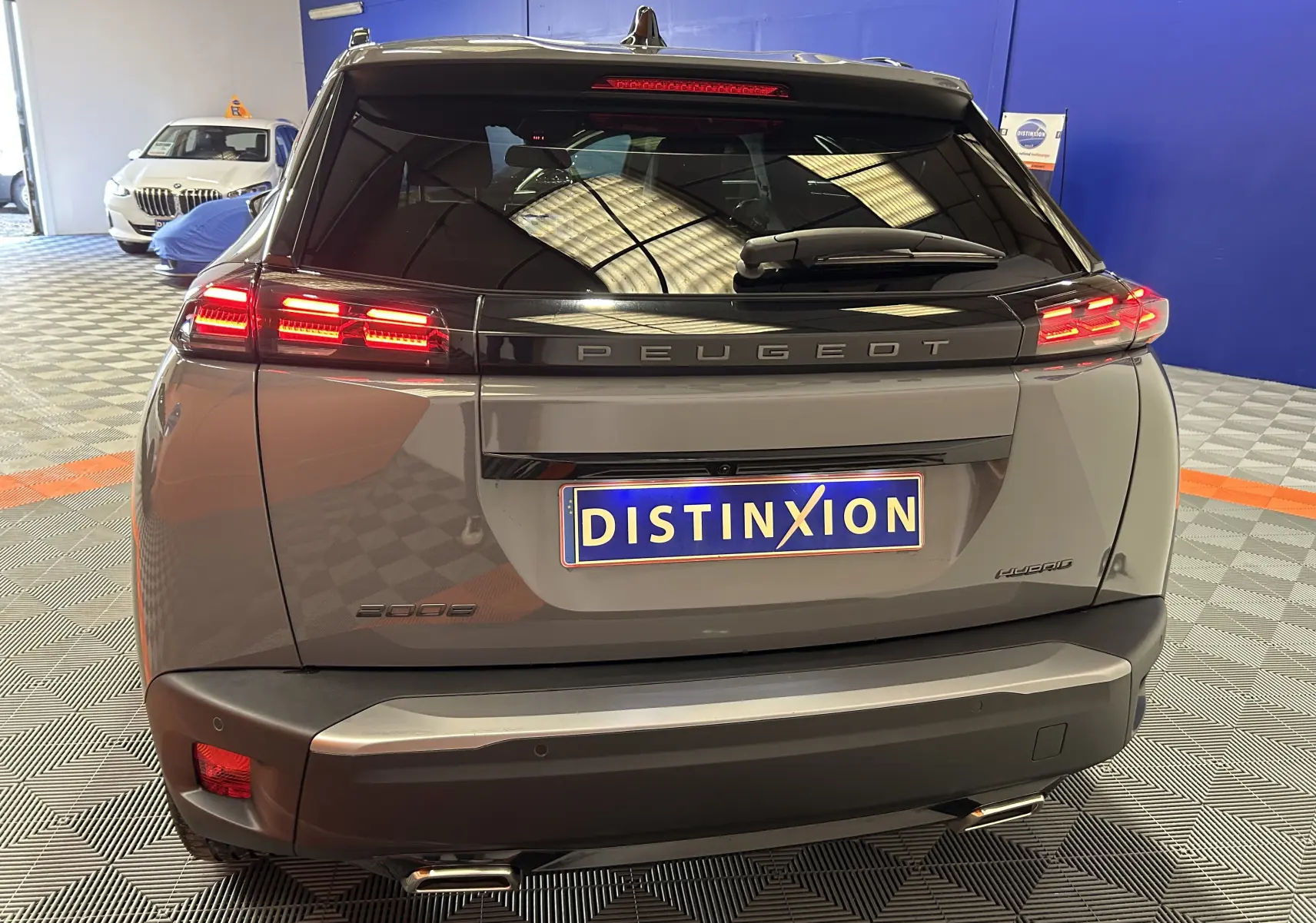 Vue arrière du Peugeot 2008 gris Selenium avec feux LED allumés et plaque d'immatriculation Distinxion en intérieur showroom.