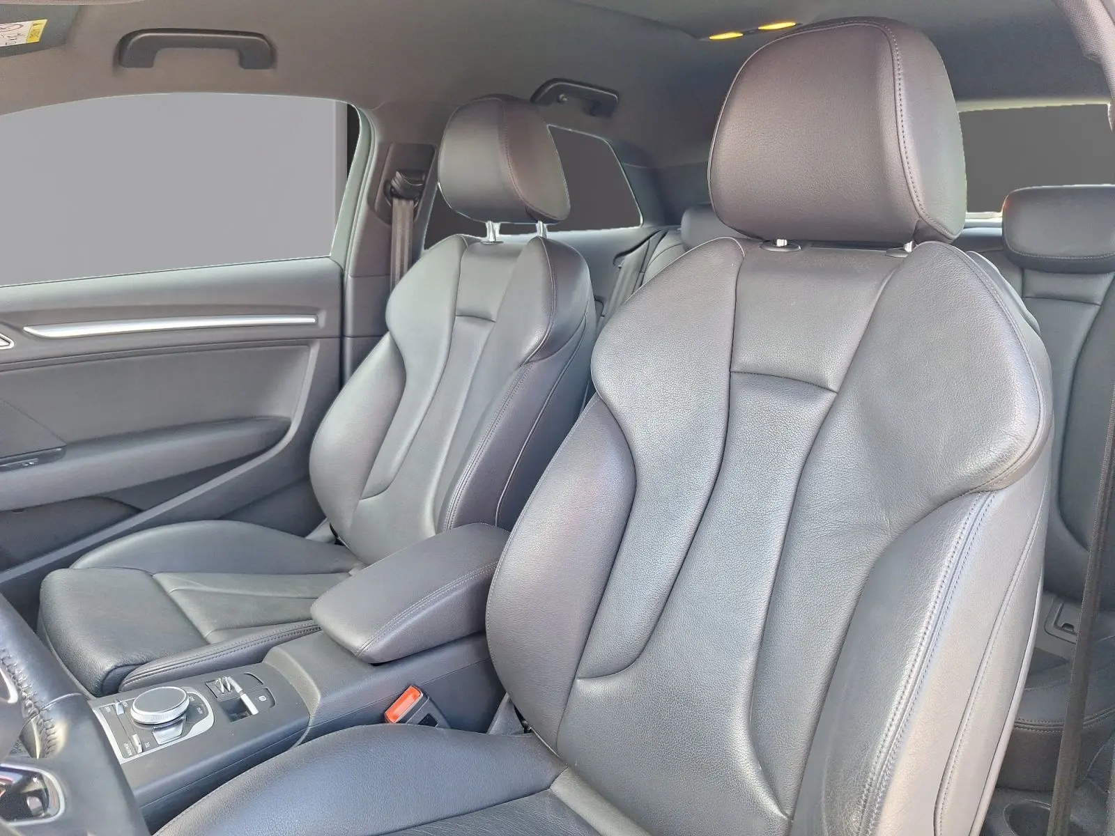 Vue intérieure des sièges avant en cuir noir de l'Audi A3 2.0 TFSI S Line, avec accoudoir central et commandes visibles.