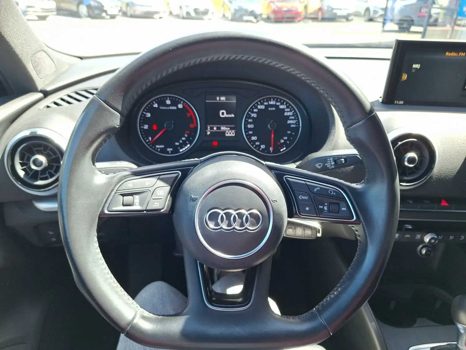 Vue intérieure centrée sur le volant cuir noir de l'Audi A3 2017 avec tableau de bord et écran multimédia visibles.
