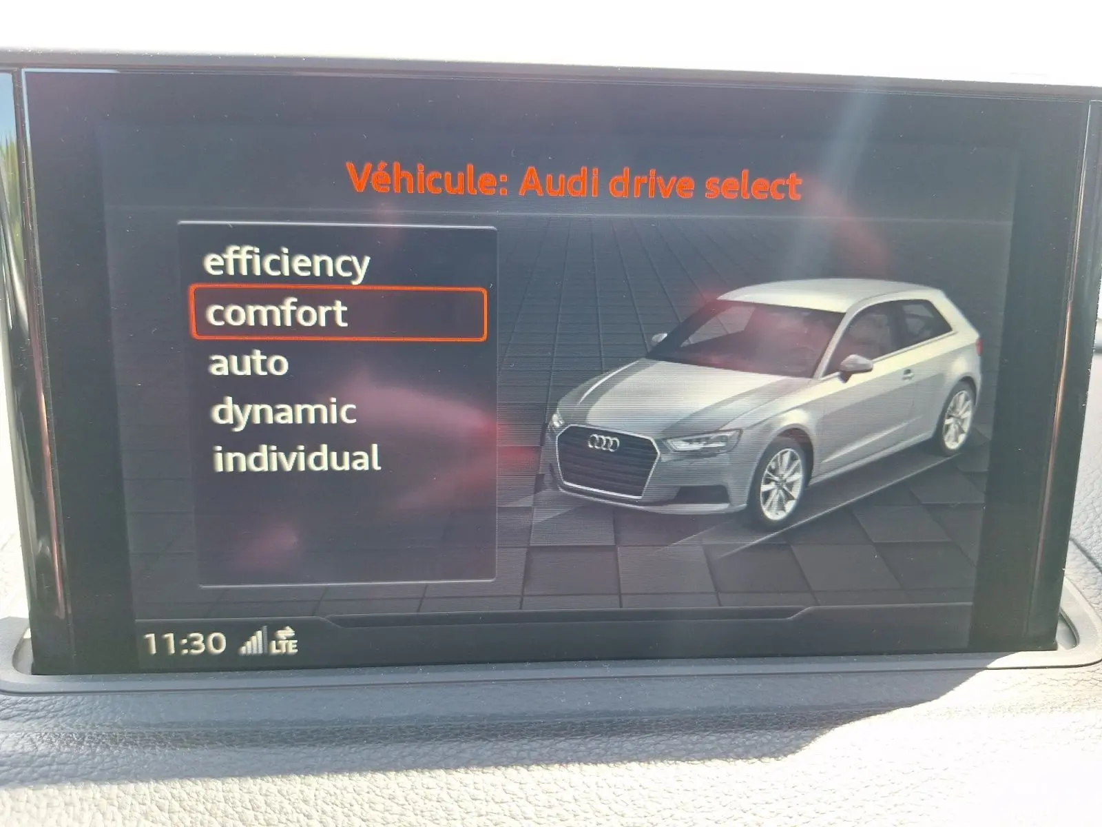 Écran intérieur montrant une Audi A3 gris clair en 3/4 avant droit avec menu de sélection mode de conduite.