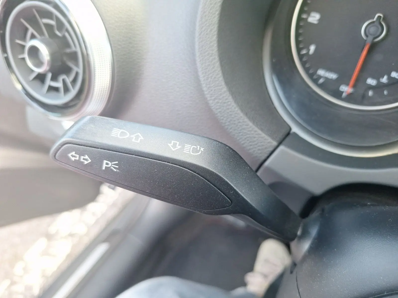 Gros plan sur la manette de clignotant noire à gauche du volant dans l’habitacle d’une Audi A3 gris 2017.