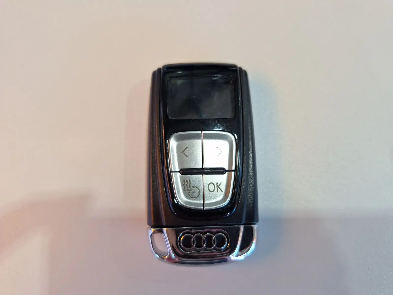 Télécommande Audi noire avec logo chromé, vue de dessus sur fond clair, boutons argentés visibles.