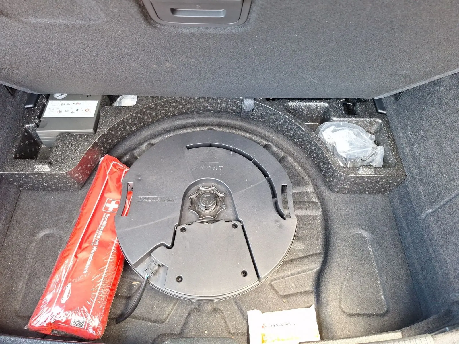 Coffre ouvert d’Audi A3 gris, vue plongeante sur la roue de secours et la trousse de secours rouge.
