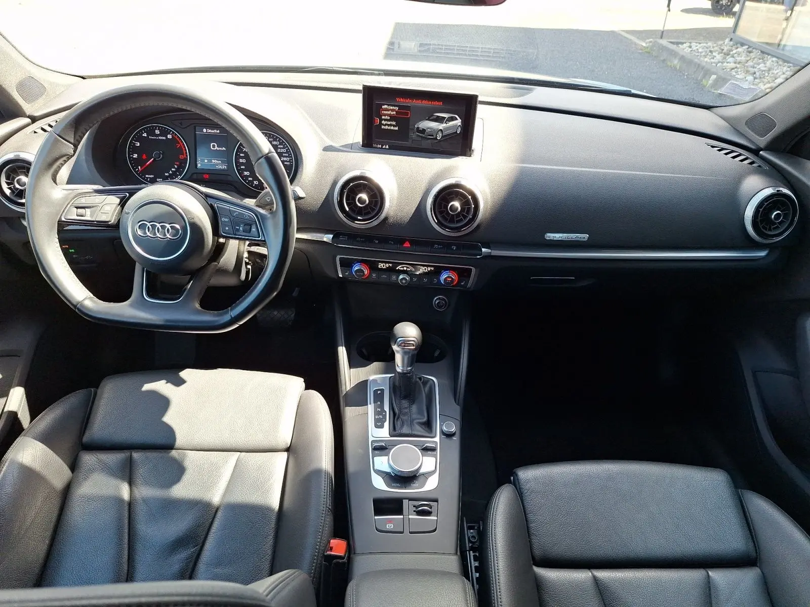 Vue intérieure avant de l'Audi A3 2017, sellerie cuir noire, tableau de bord avec écran central et volant multifonction.