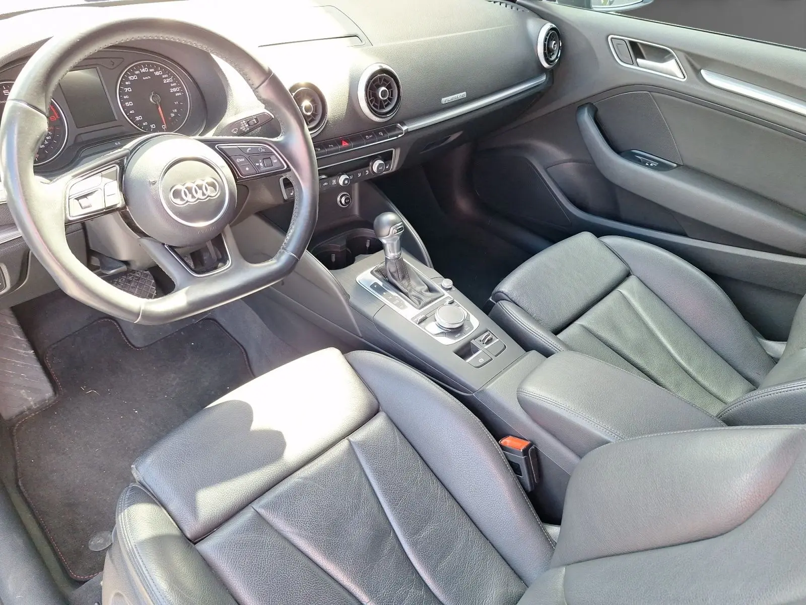 Vue intérieure côté conducteur de l'Audi A3 2017, sellerie cuir noire et console centrale avec levier de boîte automatique.