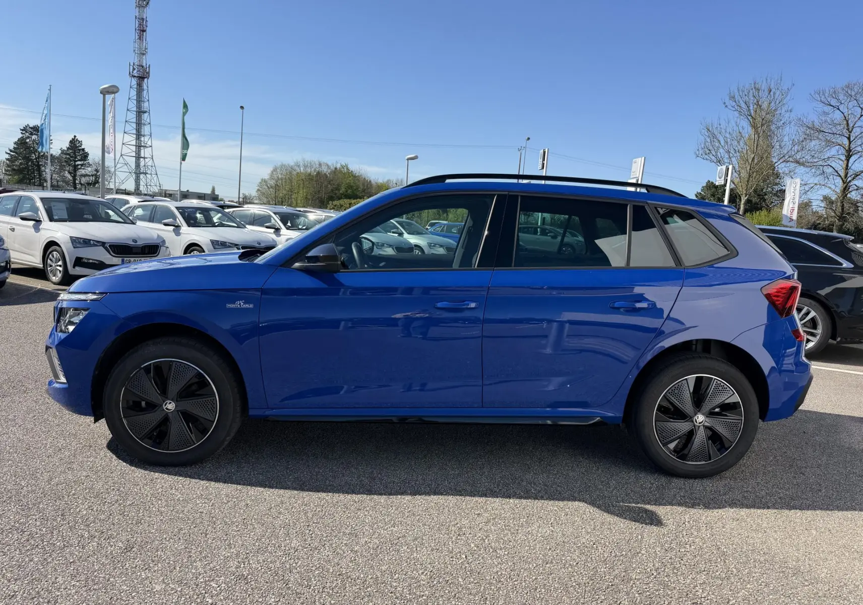 Vue de profil côté gauche d'un Skoda Kamiq bleu avec jantes alliage noires et toit ouvrant panoramique.