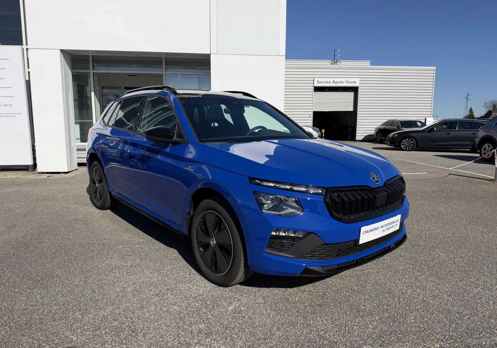 Vue 3/4 avant d'un Skoda Kamiq bleu avec calandre noire et jantes alliage noires sur parking extérieur.