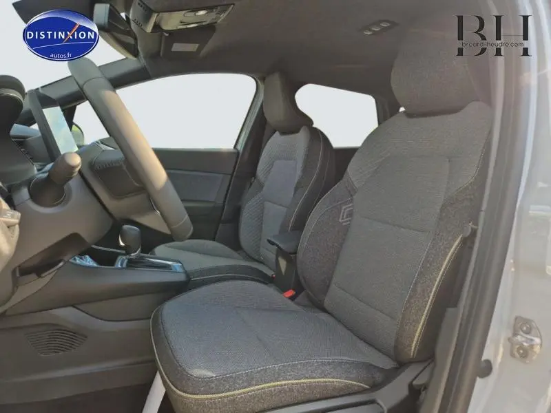 Vue intérieure côté conducteur du Renault Captur 2025, sièges tissu gris avec accoudoir central et volant multifonction.