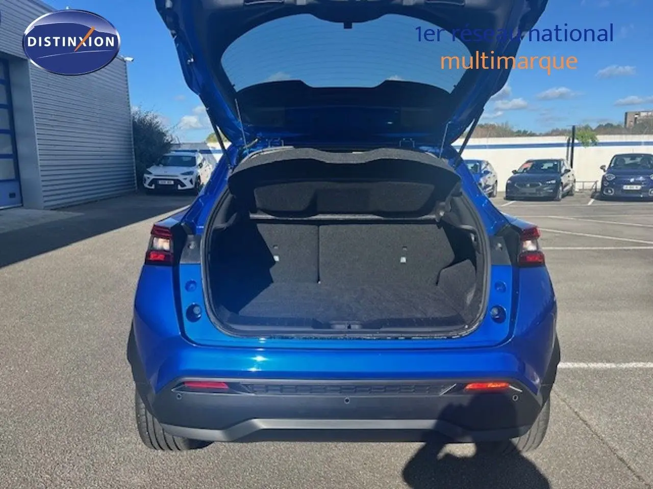 Vue arrière d'un Nissan Juke 2025 bleu magnétique métal avec coffre ouvert, montrant l'espace de chargement vide.