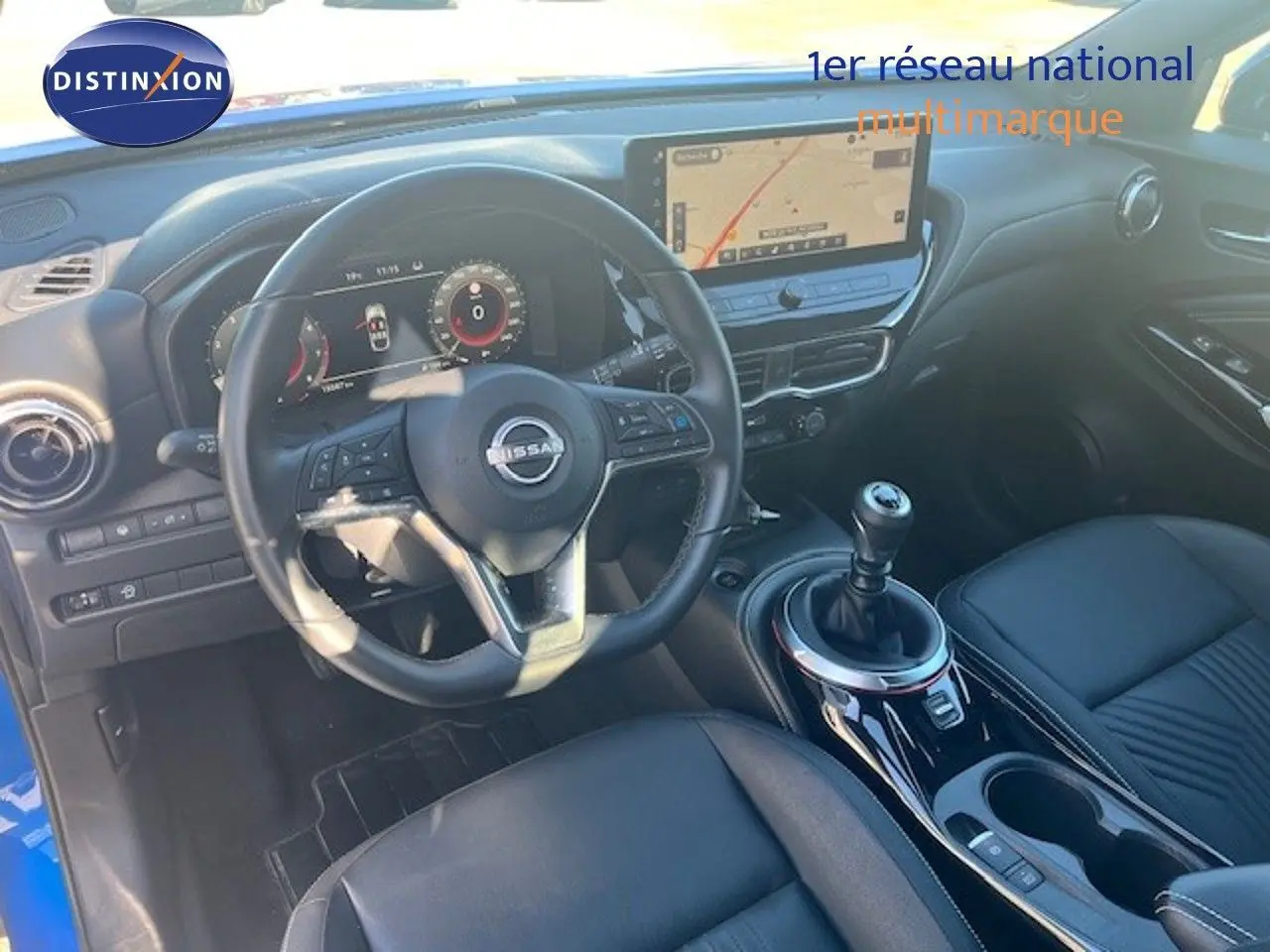 Vue intérieure du poste de conduite du Nissan Juke 2025 bleu magnétique, avec volant cuir et levier de vitesse manuel.