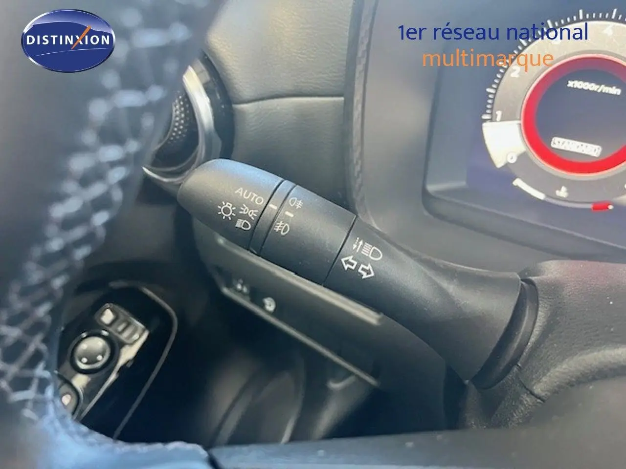 Gros plan sur la commande des feux et clignotants à gauche du volant dans un Nissan Juke bleu magnétique 2025.