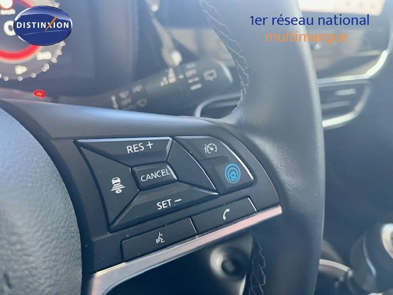 Gros plan sur les commandes au volant noir du Nissan Juke bleu magnétique, avec affichage partiel du tableau de bord.