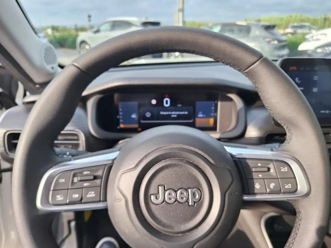 Vue rapprochée du volant noir du Jeep Avenger 2025 avec commandes intégrées et tableau de bord numérique en arrière-plan.