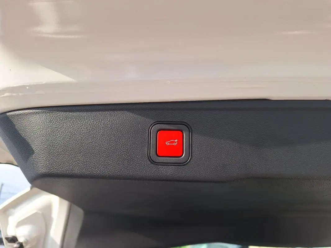 Bouton rouge d'ouverture électrique du coffre sur la partie intérieure du hayon d'un Jeep Avenger blanc.