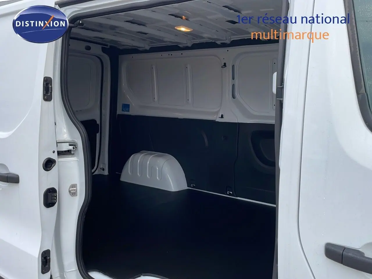 Vue intérieure du fourgon Renault Trafic blanc glacier, montrant l'espace de chargement vide et les portes latérales ouvertes.