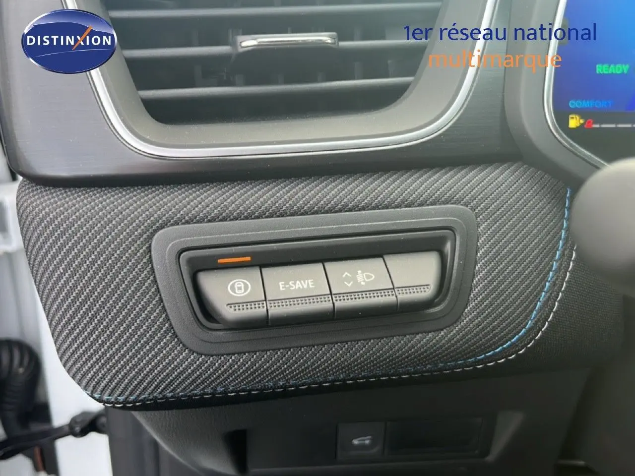 Détail intérieur montrant les boutons de commande sur un panneau en tissu carbone avec surpiqûres bleues dans une Renault Symbioz blanc nacré.