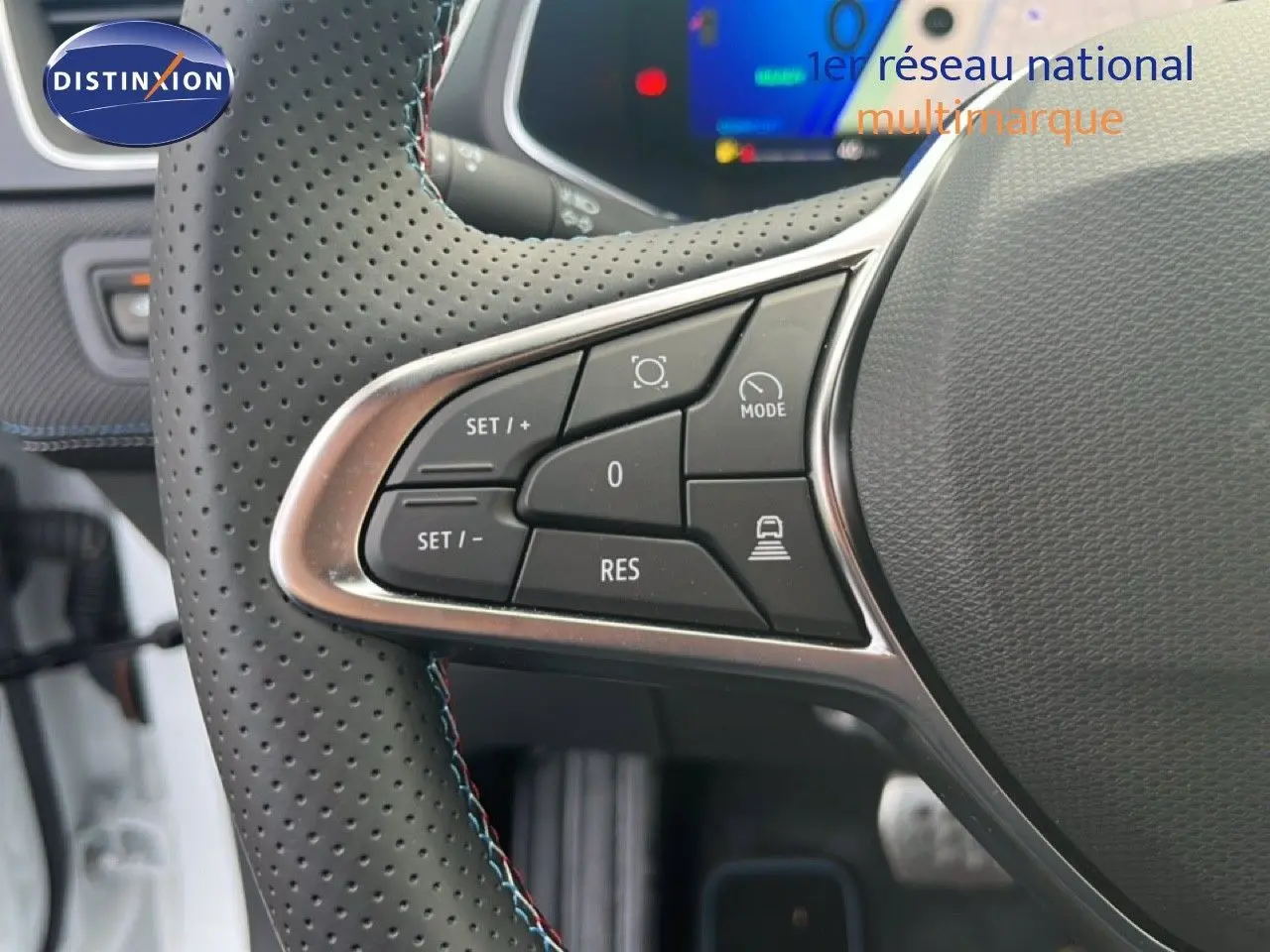 Gros plan sur la partie gauche du volant perforé du Renault Symbioz blanc nacré, avec commandes de régulateur de vitesse.