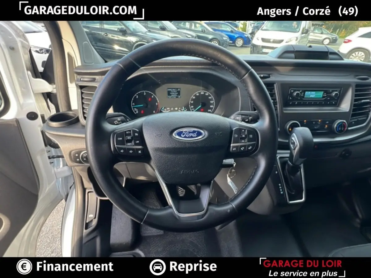 Vue intérieure centrée sur le volant en cuir noir du Ford Transit Custom 2023, avec tableau de bord et levier de vitesses automatique.