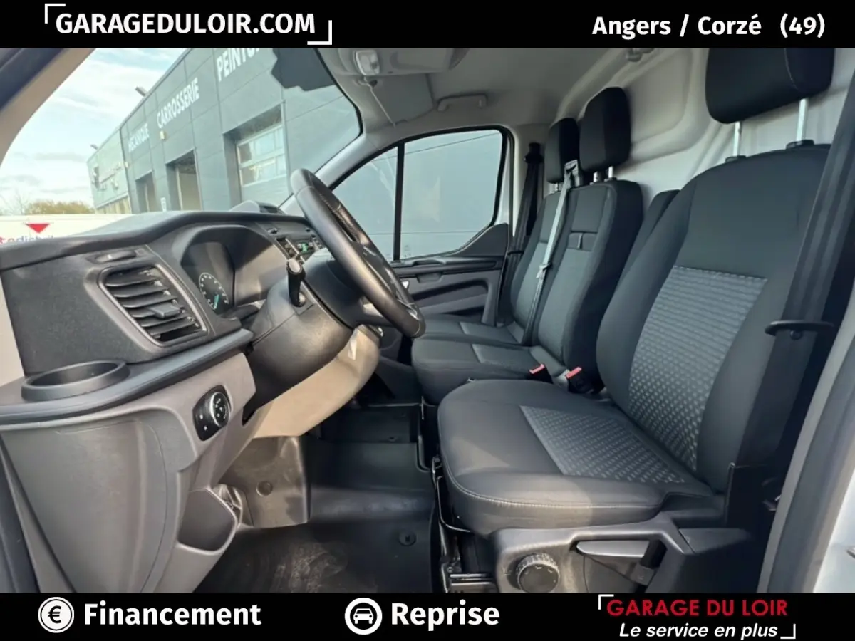 Vue intérieure côté conducteur du Ford Transit Custom blanc, montrant les sièges avant et le volant multifonction en cuir.