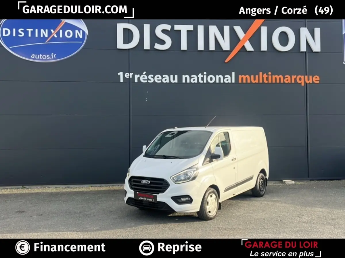 Vue 3/4 avant d'un fourgon Ford Transit Custom blanc garé devant un mur gris avec logo Distinxion.