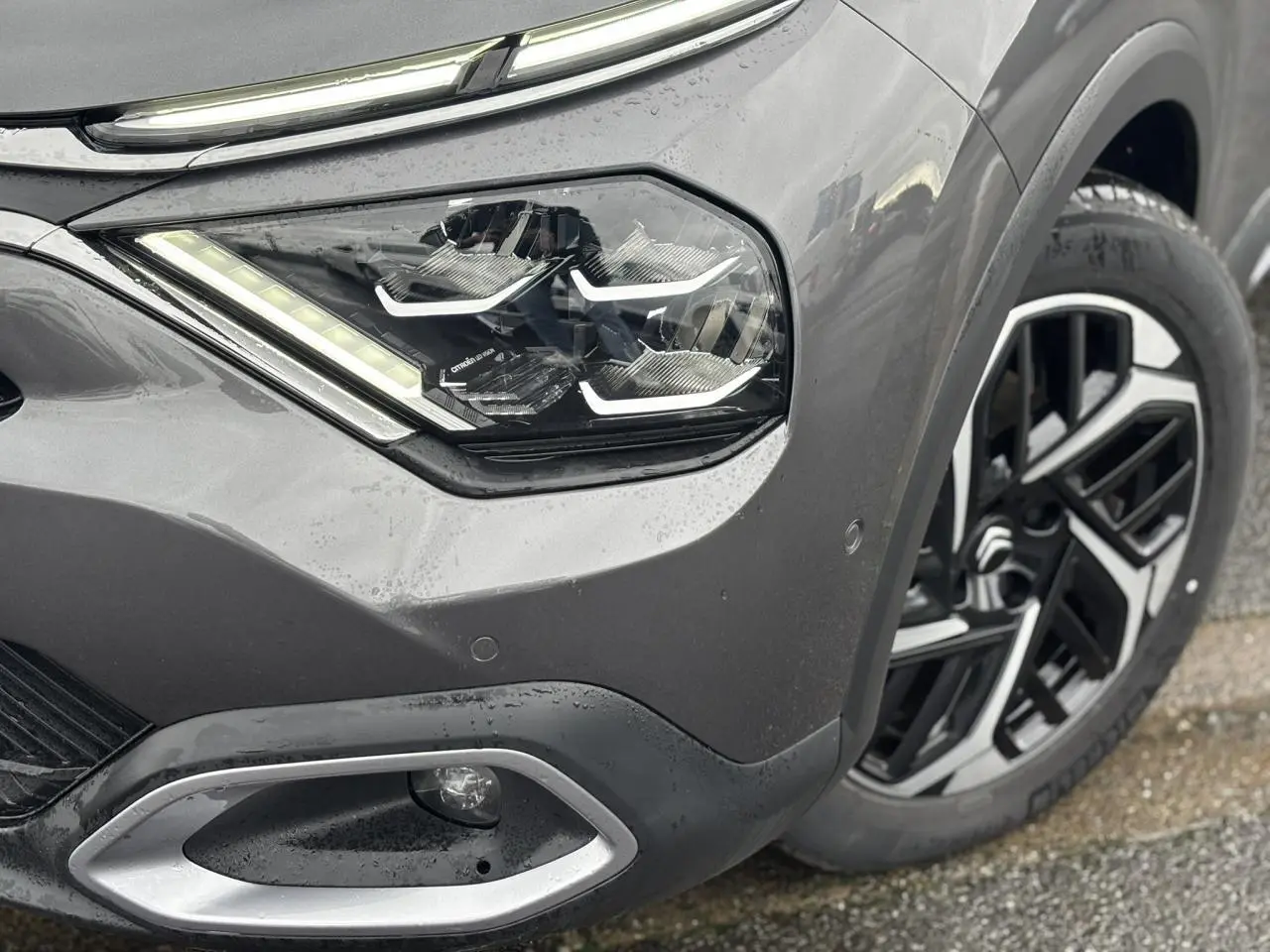 Gros plan sur l'avant droit gris Platinium du Citroën C4 2024, mettant en valeur le phare LED et la jante alliage 18 pouces.