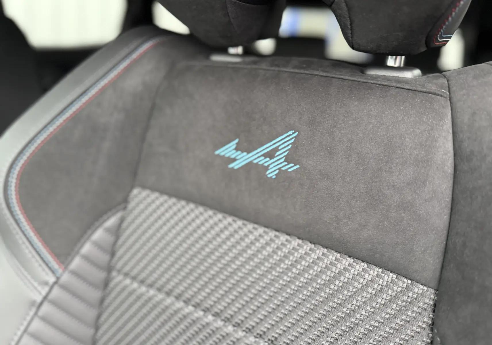 Gros plan sur le siège avant en tissu gris et alcantara avec logo Alpine bleu et surpiqûres tricolores.