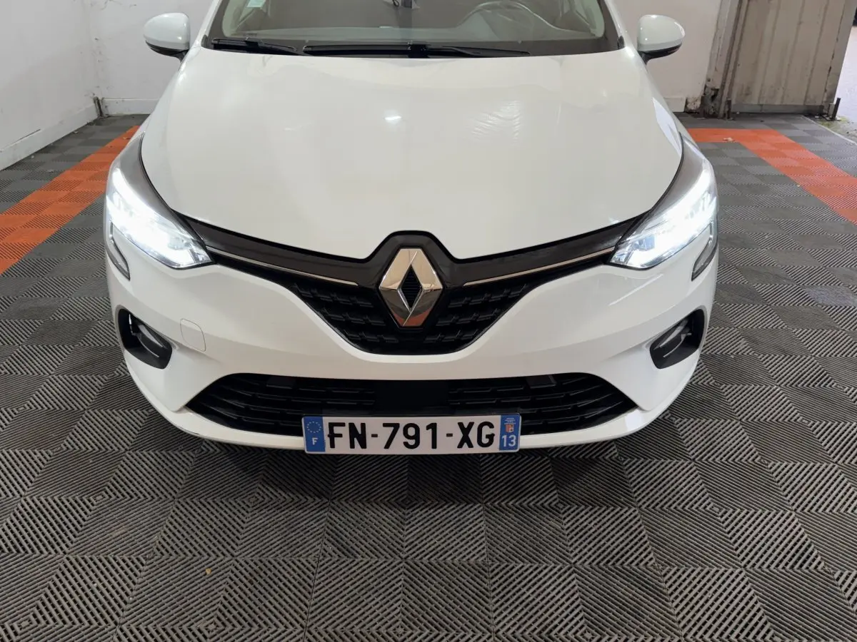 Vue avant d'une Renault Clio Business TCe 100 blanche avec phares LED allumés et calandre noire brillante.