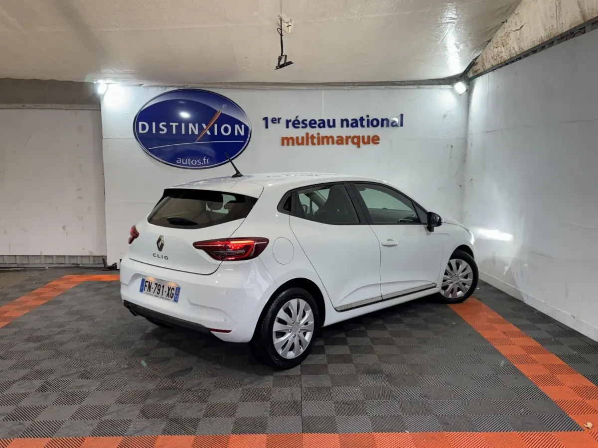 Renault Clio Business TCe 100 blanche vue 3/4 arrière droit dans un showroom avec logo Distinxion en arrière-plan.