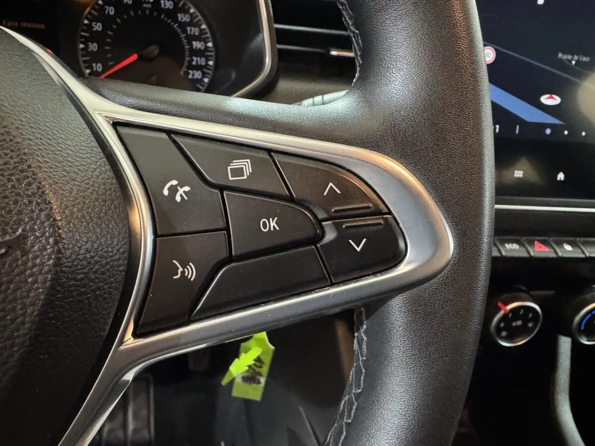 Gros plan sur les commandes multifonctions du volant cuir noir de la Renault Clio Business TCe 100, avec tableau de bord partiel visible.