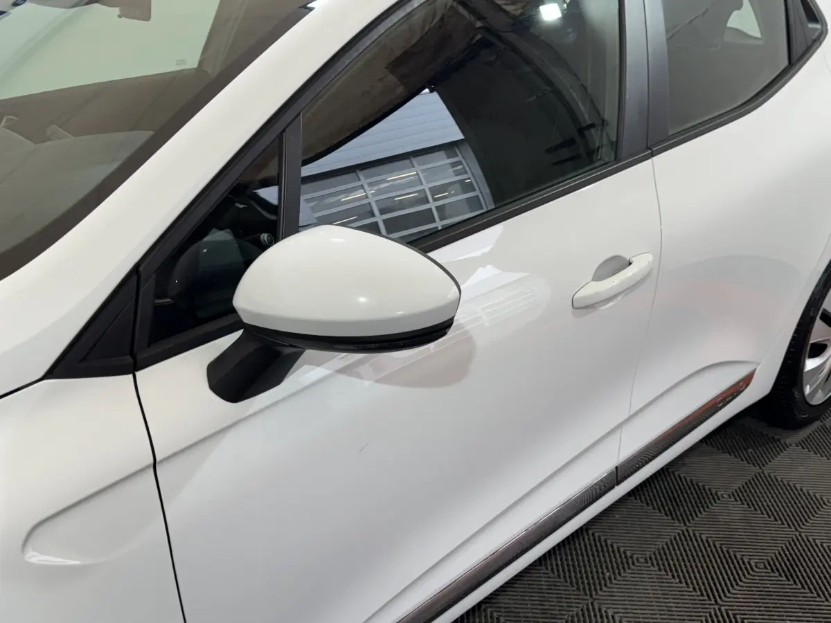 Vue latérale droite rapprochée d'une Renault Clio Business TCe 100 blanche avec rétroviseur blanc et poignée de porte visible.