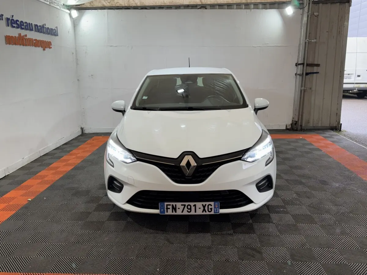 Renault Clio Business TCe 100 blanche vue de face, phares LED allumés dans un garage éclairé.