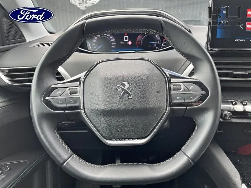 Vue rapprochée du volant cuir noir multifonction d’un Peugeot 5008 2021 avec tableau de bord digital.