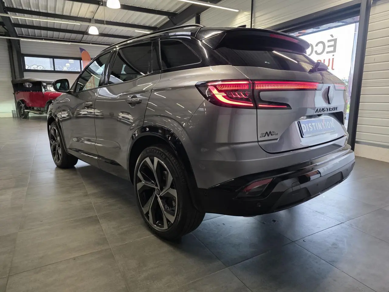 Vue 3/4 arrière droite d'un Renault Austral gris foncé avec jantes alliage 20 pouces et toit noir étoilé en intérieur showroom.