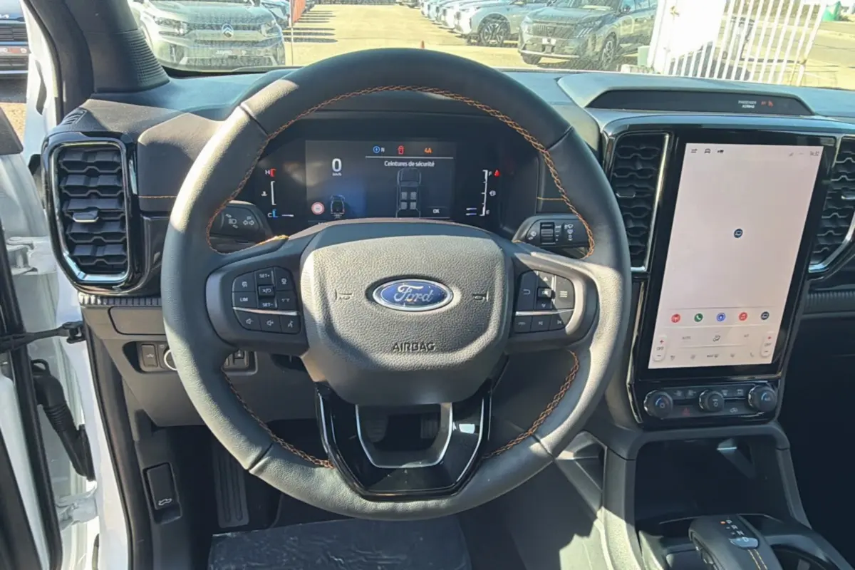 Vue intérieure centrée sur le volant cuir multifonctions avec coutures orange du Ford Ranger blanc, écran tactile vertical visible.