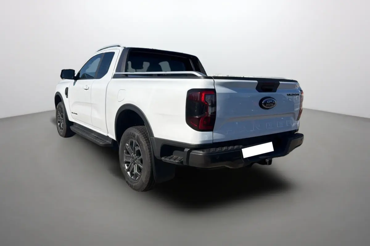 Ford Ranger Wildtrak blanc pur vu en 3/4 arrière gauche avec arceau sport et barres de toit visibles.