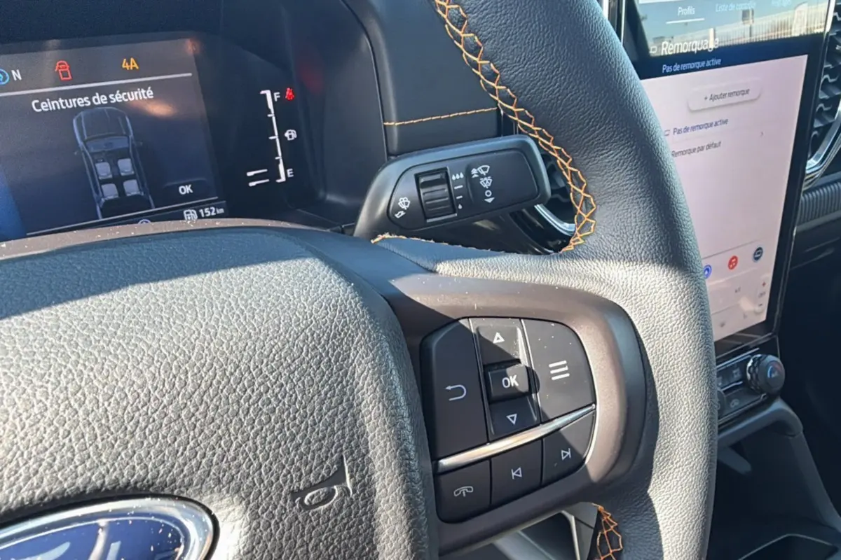 Gros plan sur le volant cuir noir avec surpiqûres orange du Ford Ranger 2025, affichage numérique et écran tactile visible.