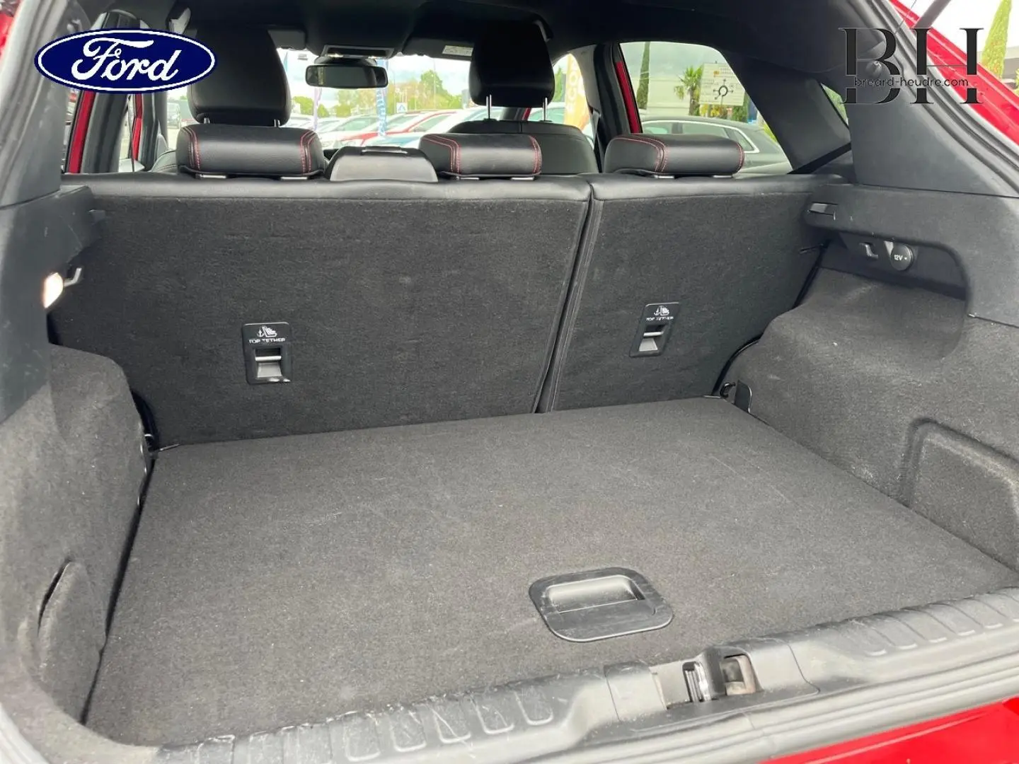 Vue du coffre ouvert du Ford Puma rouge Premium Lucid, montrant la banquette arrière rabattable et l'espace de chargement.