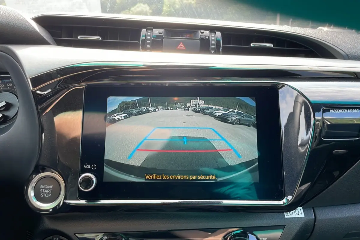 Vue de l'écran de recul du Toyota Hilux 4x4 blanc 2025, version Invincible, avec caméra arrière et commandes au tableau de bord.