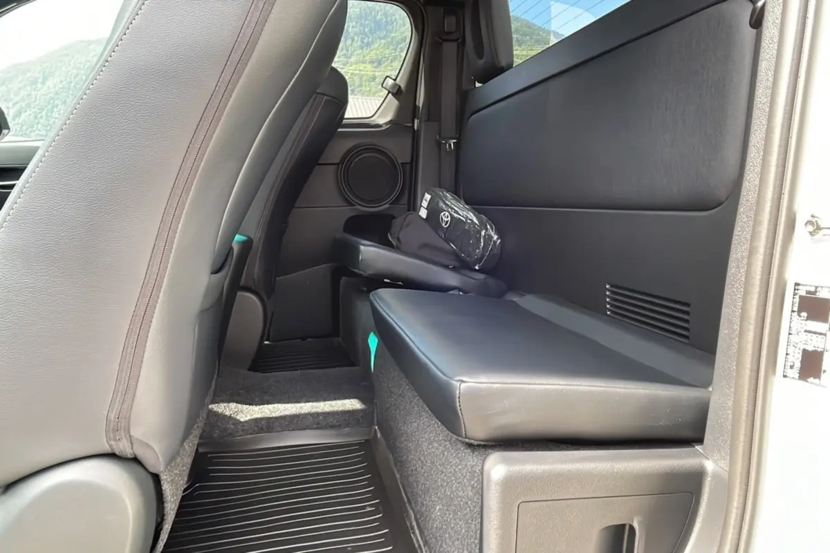 Vue intérieure arrière côté droit du Toyota Hilux 4x4 blanc 2025, siège rabattable en cuir noir et rangement avec trousse Toyota.