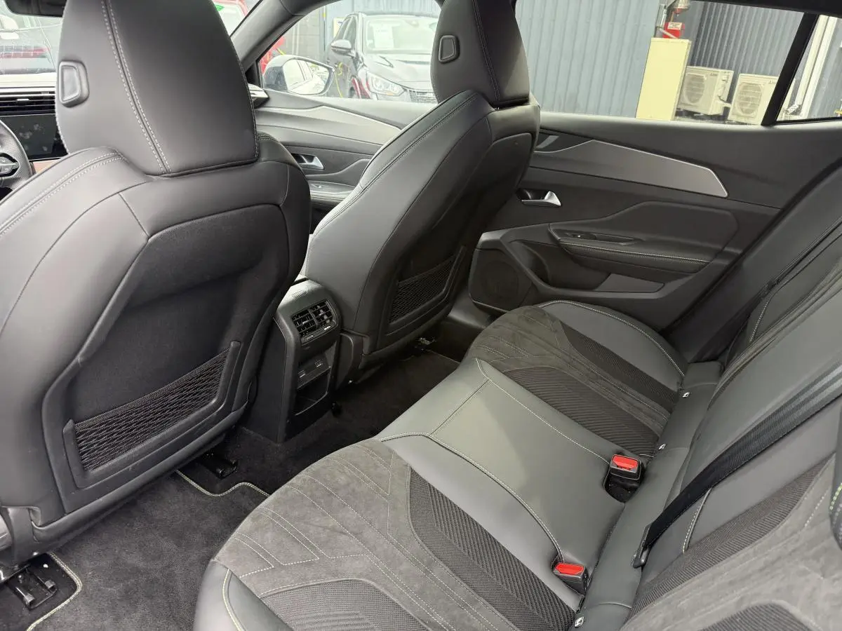 Vue arrière intérieure de la Peugeot 408 2024, sièges arrière en tri-matière gris avec surpiqûres vertes et aérations centrales.