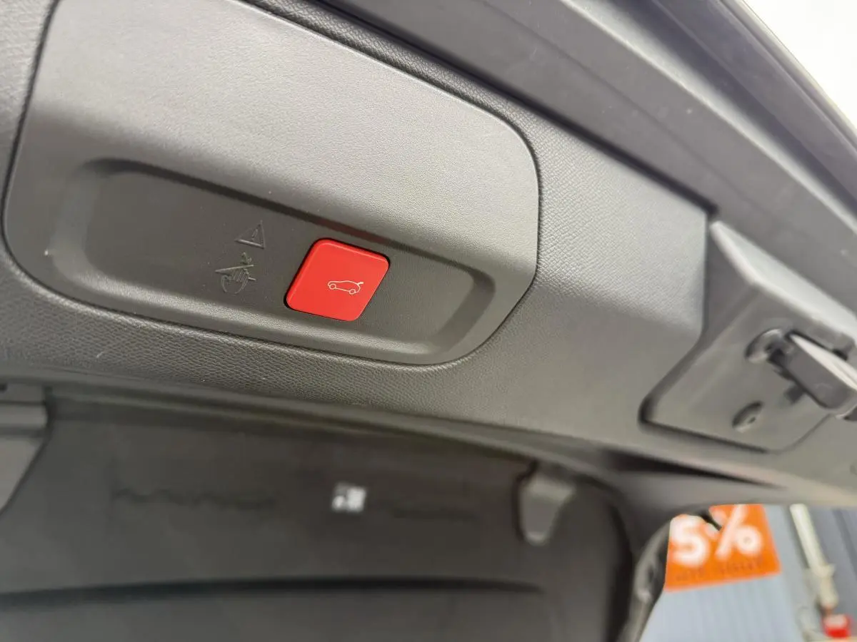 Bouton rouge d'ouverture motorisée du hayon sur le bord intérieur du coffre d'une Peugeot 408 blanche 2024.