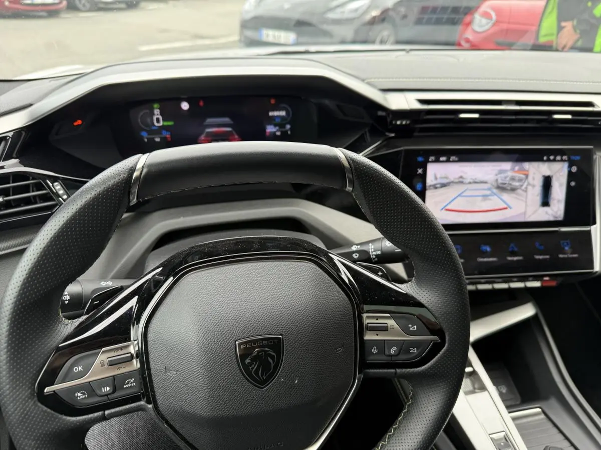 Vue rapprochée du volant cuir perforé noir et du tableau de bord numérique de la Peugeot 408 blanche 2024.