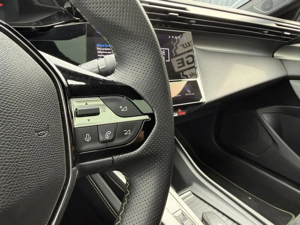 Gros plan sur le volant noir perforé avec commandes intégrées et tableau de bord moderne du Peugeot 408 blanc 2024