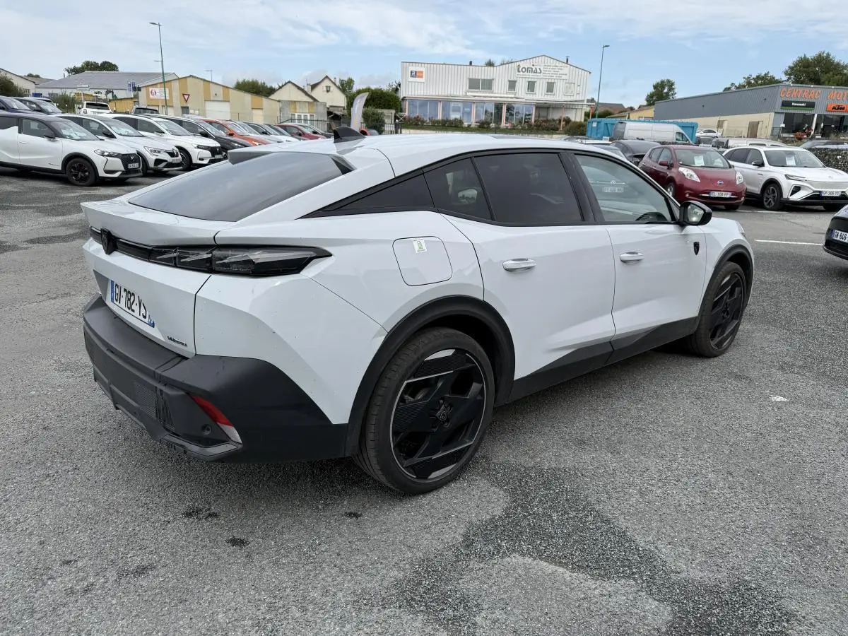 Vue 3/4 arrière droite d'une Peugeot 408 blanche avec jantes noires et toit noir Mistral sur parking extérieur.