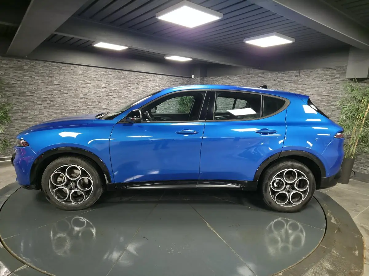 Vue de profil côté gauche d'un Alfa Romeo Tonale bleu métallisé avec jantes alliage 18 pouces dans un showroom.