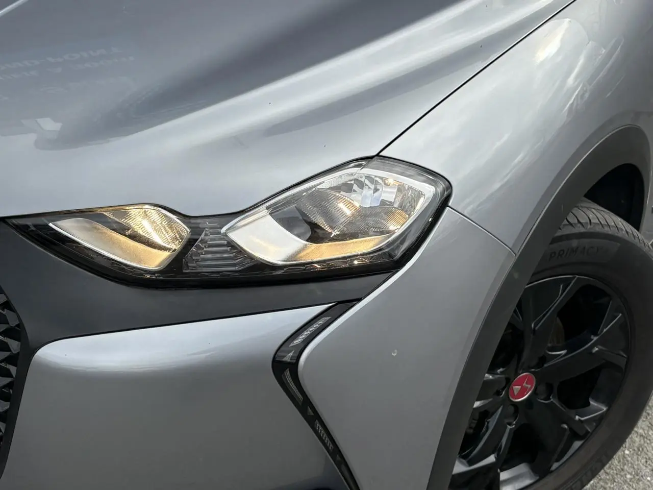 Gros plan sur le phare avant droit et la roue noire du DS3 Crossback gris Artense, mettant en valeur le design anguleux.