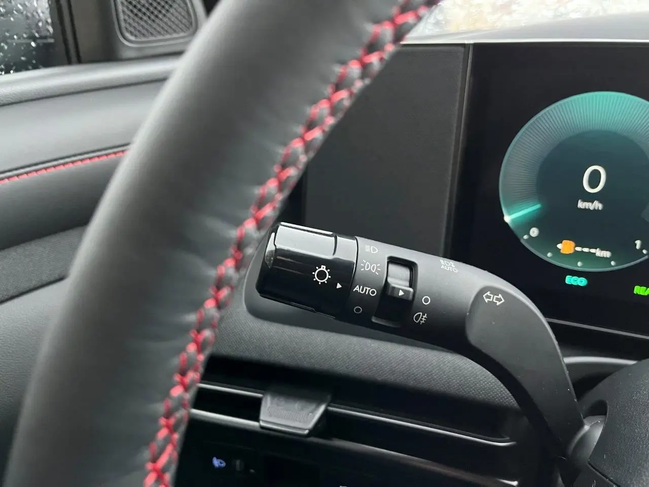 Vue rapprochée du commodo d’éclairage à gauche du volant noir avec surpiqûres rouges dans l’habitacle du Hyundai Tucson 2025.